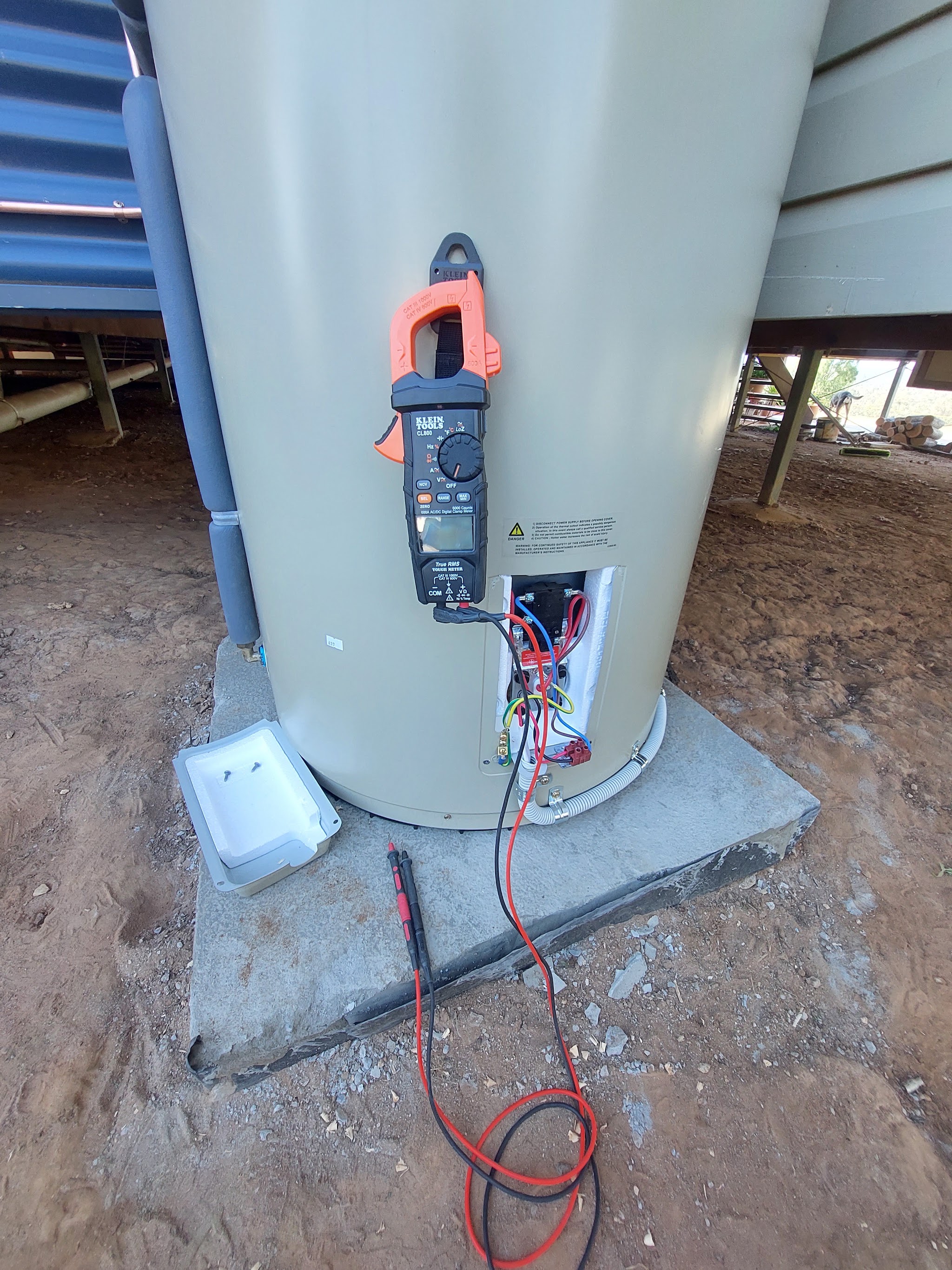 Testing a hot water unit with a clamp meter under a rural home